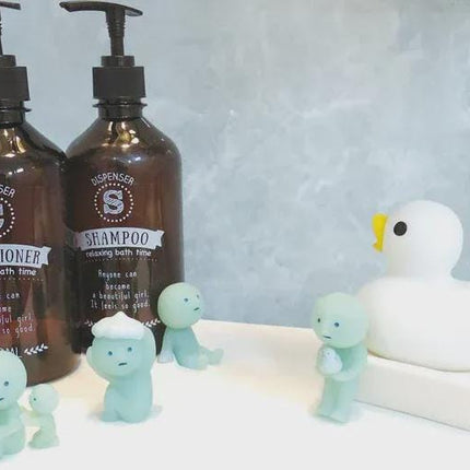 two brown bottles of conditioner and shampoo, along with a white rubber duck and several small green figures, all arranged on a white surface against a blue background.