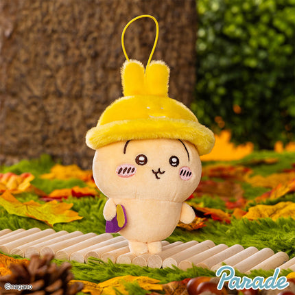 Autumn mascot plush with yellow bunny-ear hood, white face, smiling eyes, dangling loop.