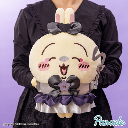 Round cream panda-like plush toy with bunny-ear black bow and purple ruffle skirt