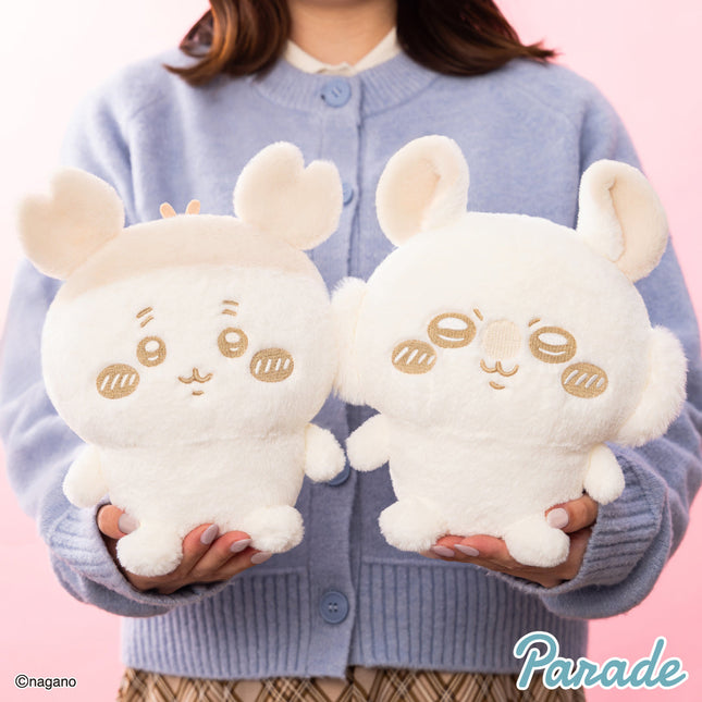 Cream plush rabbit character pair, held by person in blue sweater; embroidered faces, long ears.