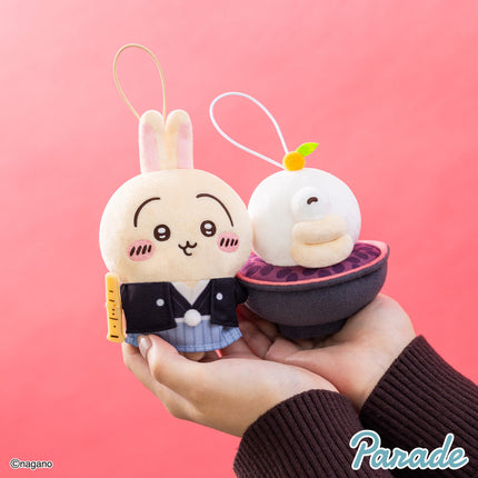 New Year mascot plush pair held in hands: bunny and white creature in black jackets