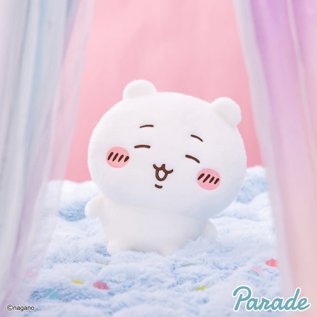 Super fluffy white plush toy with closed-eye face and rounded ears, sitting on soft fabric