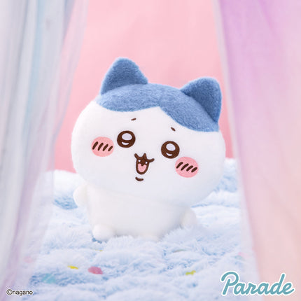 Super fluffy white plush toy with blue ears and an embroidered sleepy face, resting on bedding