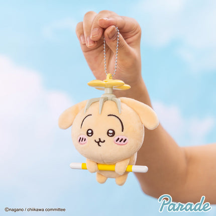 Plush mascot keychain held by hand, tan character with small sword-like prop and chain