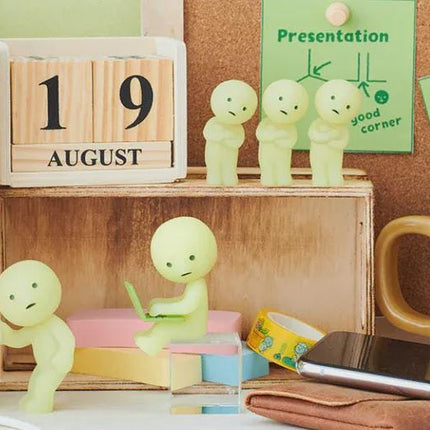 a desk with various objects, including a calendar, a mug, a smartphone, and several small figurines. The objects are arranged in a casual manner, creating a relaxed and informal setting.