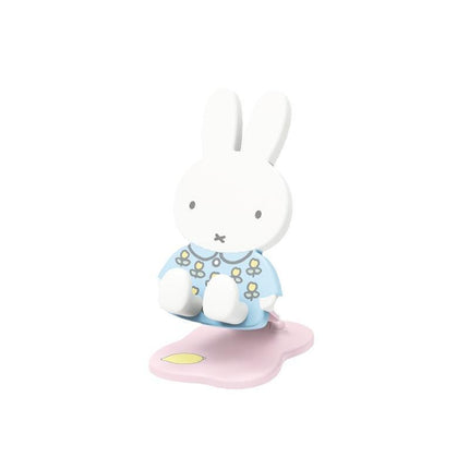 A white bunny figurine wearing a blue shirt with yellow flowers, sitting on a pink base.