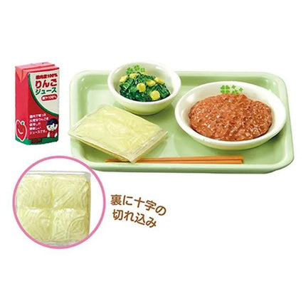 a tray with various food items, including a bowl of soup, a plate of noodles, and a small bowl of vegetables. There is also a carton of juice on the tray.