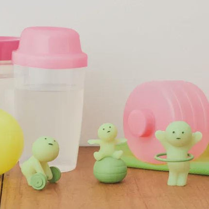 a collection of fitness-related items, including a pink water bottle, a yellow ball, a green hula hoop, and two small green figurines.