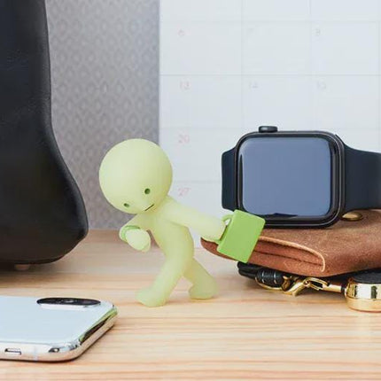 a desk with various items, including a black leather bag, a small figurine, a watch, a phone, and a wallet.