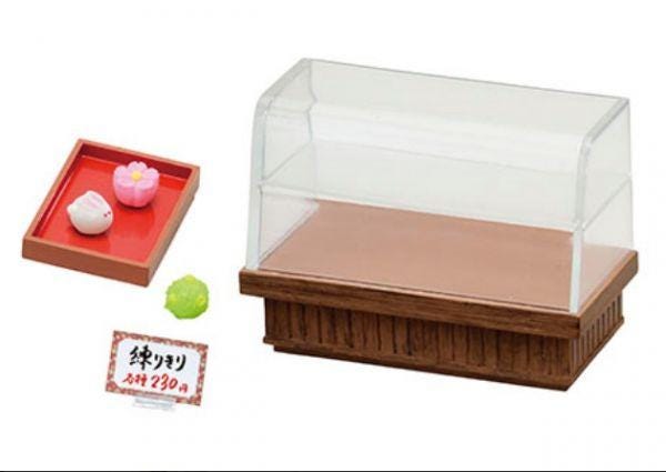 a toy store display with a clear glass case, a red tray, and a small green frog toy.