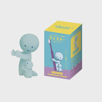 A small figurine of a smiling baby holding a toothbrush, and a toothbrush stand box with a cartoon image of a baby and a toothbrush.
