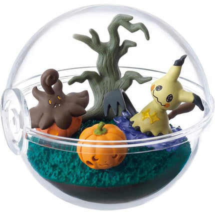 A Halloween-themed glass terrarium containing a pumpkin, a monster, and a tree.
