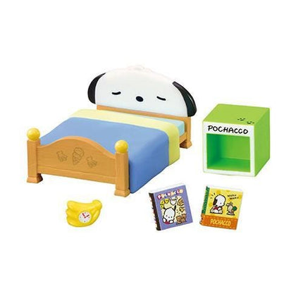 A Snoopy-themed bed with a blue and yellow striped blanket, a green box labeled "POCACCO", and a banana-shaped alarm clock.