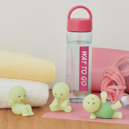 a pink water bottle with a "Way to Go" label, surrounded by various fitness-related items such as a yellow towel, a pink exercise mat, and three small green figurines.