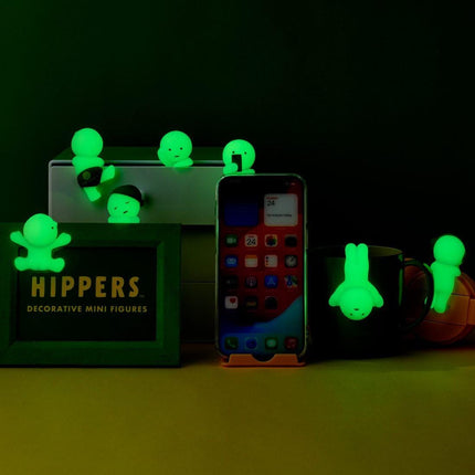 a collection of miniature figurines, including a framed item with the word "HIPPERS" and a smartphone, all illuminated by green light.