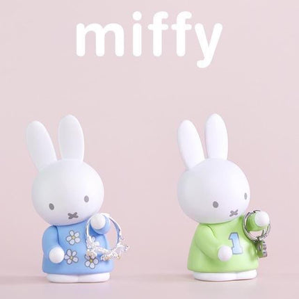 two cute white bunny figurines, one wearing a blue dress and the other wearing a green shirt with a number 1 on it, standing on a pink background.