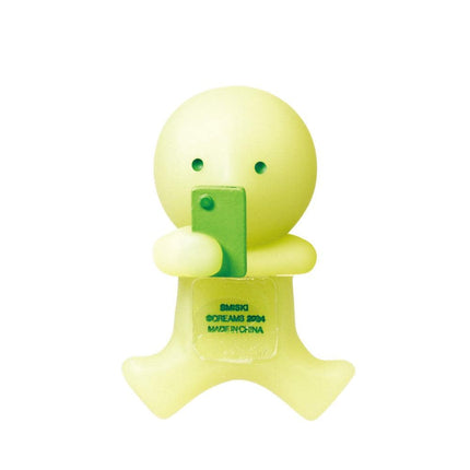 A yellow figurine holding a green object, possibly a phone, and displaying the text "SMISKI SOLEIMA 2014 MADE IN CHINA" on its body.
