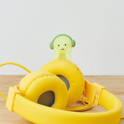 A pair of yellow headphones with a small green ghost figurine perched on top of them.