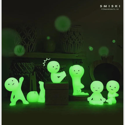A group of glowing green figurines, resembling small human-like figures, are arranged on a surface in a dark room.