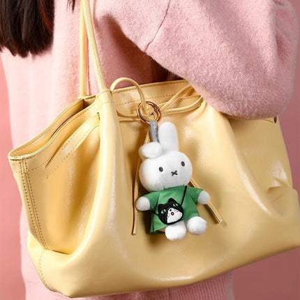 May include: A yellow leather handbag with a small white plush bunny keychain. The bunny wears a green shirt with a black cat graphic. The bag has a drawstring closure and a shoulder strap.