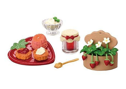 various food items and utensils, including a plate with pastries, a glass bowl with cream, a jar with a lid, a small cake with strawberries, and a small cake with a heart-shaped plate.