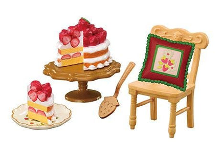 a cake with strawberries on top, a wooden chair with a red and green pillow, and a small plate with a slice of cake.