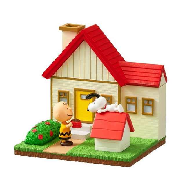 A toy figurine of a character from the Peanuts comic strip standing in front of a small house with a red roof.