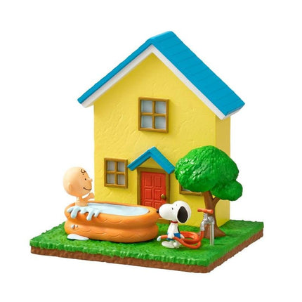 A miniature model of a yellow house with a blue roof, featuring a small tree and a toy character, likely representing the Peanuts characters.