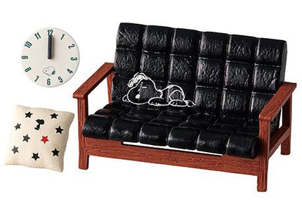A black leather couch with a cartoon character drawn on it, a white clock, and a small pillow with stars on it.