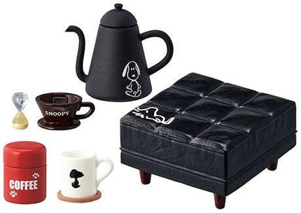 a variety of objects, including a black coffee pot, a Snoopy mug, a red coffee can, a black leather ottoman, and a Snoopy-themed coffee cup.