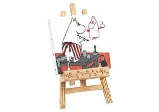 A small wooden easel with a painting of a cartoon character, likely Moomoo, sitting at a table and drawing a picture of another character.