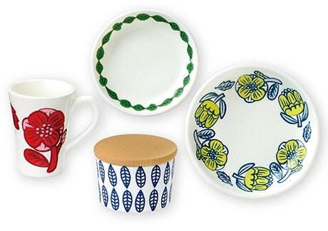 a collection of four ceramic items, including a white mug with a red flower design, a white plate with a blue and yellow floral design, a white bowl with a blue leaf pattern, and a white plate with a yellow flower design.