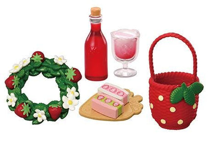 a wreath, a bottle of red liquid, a glass of pink liquid, a red basket with a green leaf, and a cake on a wooden board.