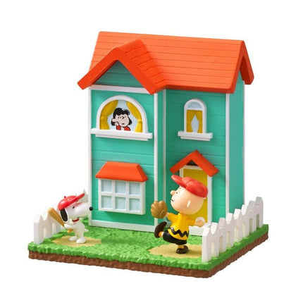 A miniature toy house with a green exterior and an orange roof, featuring a small figure of a baseball player and a dog.