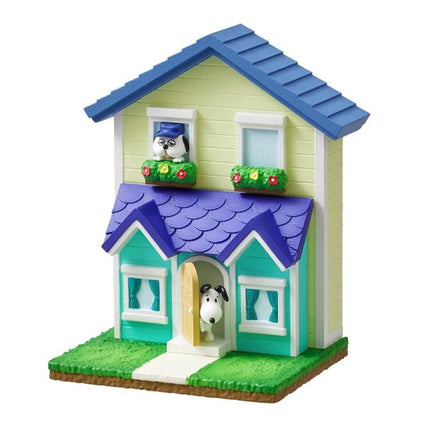 A small, colorful toy house with a blue roof, yellow walls, and a brown door. The house has two windows, one on each side, and a small dog figurine is visible inside the house.
