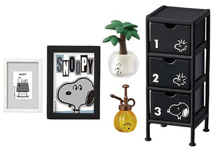 a collection of various items related to the character Snoopy, including a framed image of Snoopy, a potted plant, a watering can, a black storage unit, and a small figurine.