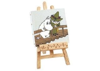 a small wooden easel with a painting of two cartoon characters, a white character and a green character, sitting together on a wooden platform.