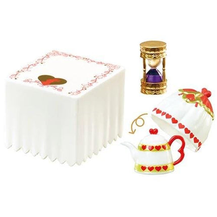 a white square cake with a heart design, a gold hourglass, and a red and white teapot with a heart design.