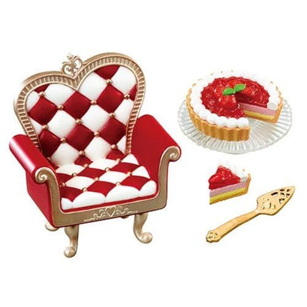 A red and white checkered chair with a gold frame, a slice of cake with red filling, and a gold serving spoon.