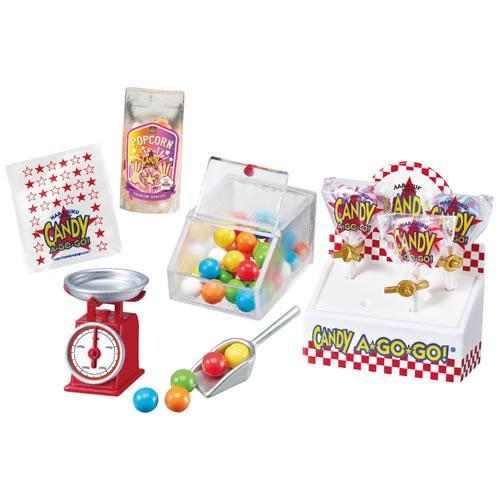 various candy-related items, including a bag of popcorn, a candy dispenser, a scale, and a container filled with colorful gummy candies.