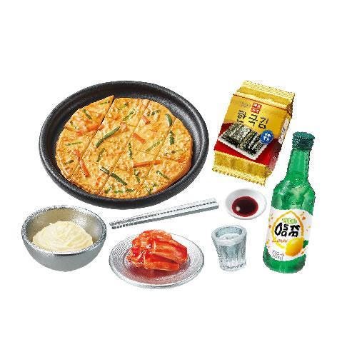 various food items and condiments, including a pizza, a green bottle, a bowl of sauce, a plate of sliced meat, a glass of water, and a small bowl of sauce.