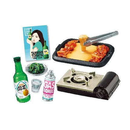 various food items and kitchen appliances, including a bottle of green sauce, a tray of food, a gas stove, a bowl of green vegetables, and a book.