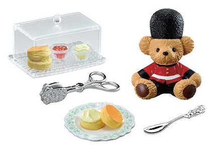 a teddy bear wearing a red coat and a black hat, a pair of silver tongs, a plate with pastries, and a spoon.