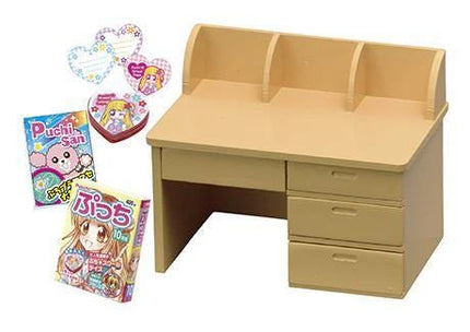 a wooden desk with three drawers, a magazine, and some stickers.