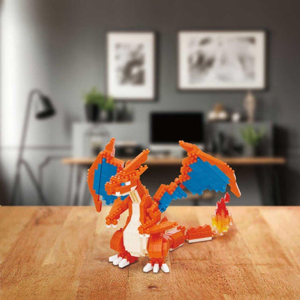 A LEGO Charizard figurine is displayed on a wooden surface, with a blurred background featuring a desk, plants, and artwork.
