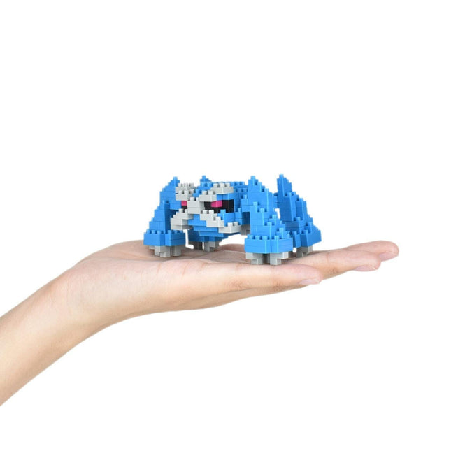 A hand holding a small blue and white toy, which appears to be a pixelated or miniature version of a character or object.