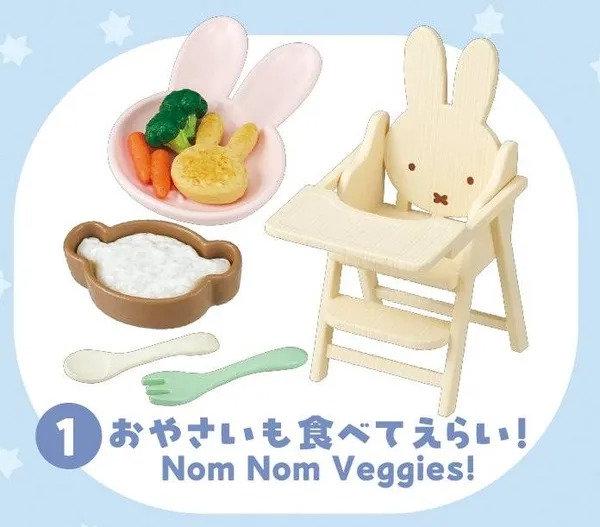 A wooden high chair with a small bowl of vegetables, a spoon, and a fork, along with a sign that says "Nom Nom Veggies!"