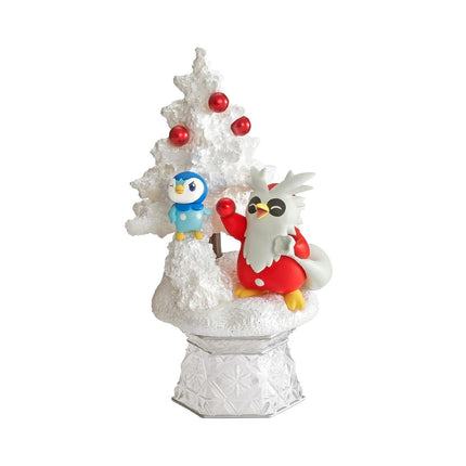 A figurine of a penguin and a bird, both wearing red and white outfits, standing on a snowy base with a Christmas tree decoration.