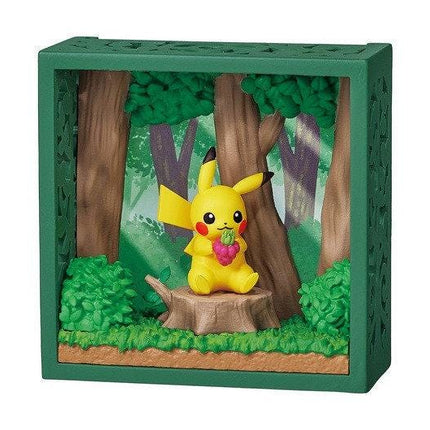 A small, green-framed diorama depicting a yellow Pikachu figurine sitting on a tree stump in a forest setting.