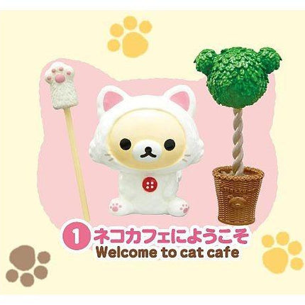 A small white cat figurine with a red button on its chest, surrounded by a cat-themed background with paw prints and a tree-shaped object.